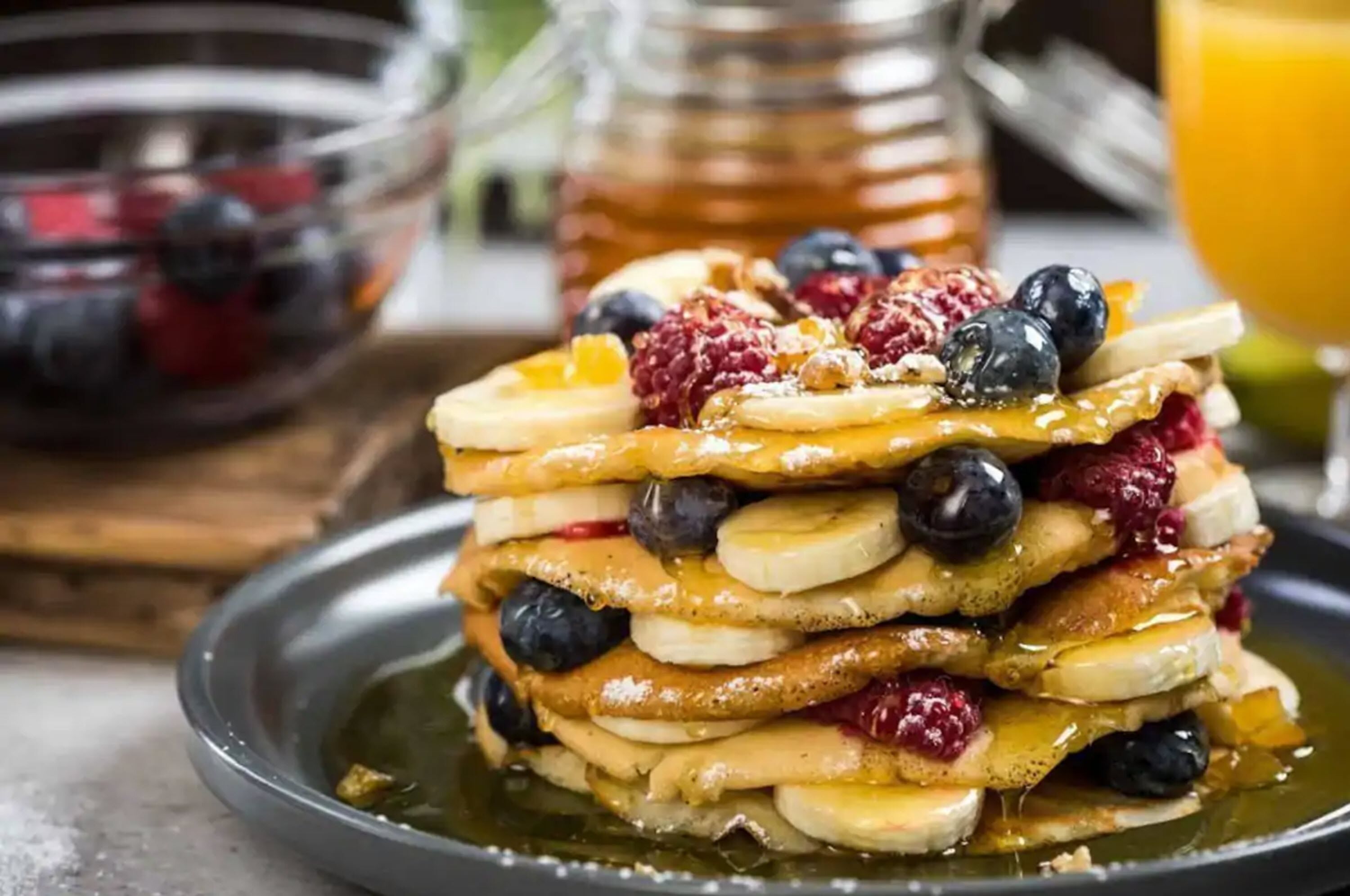 A stack of pancakes with blueberries, raspberries, and banana slices, served with syrup.