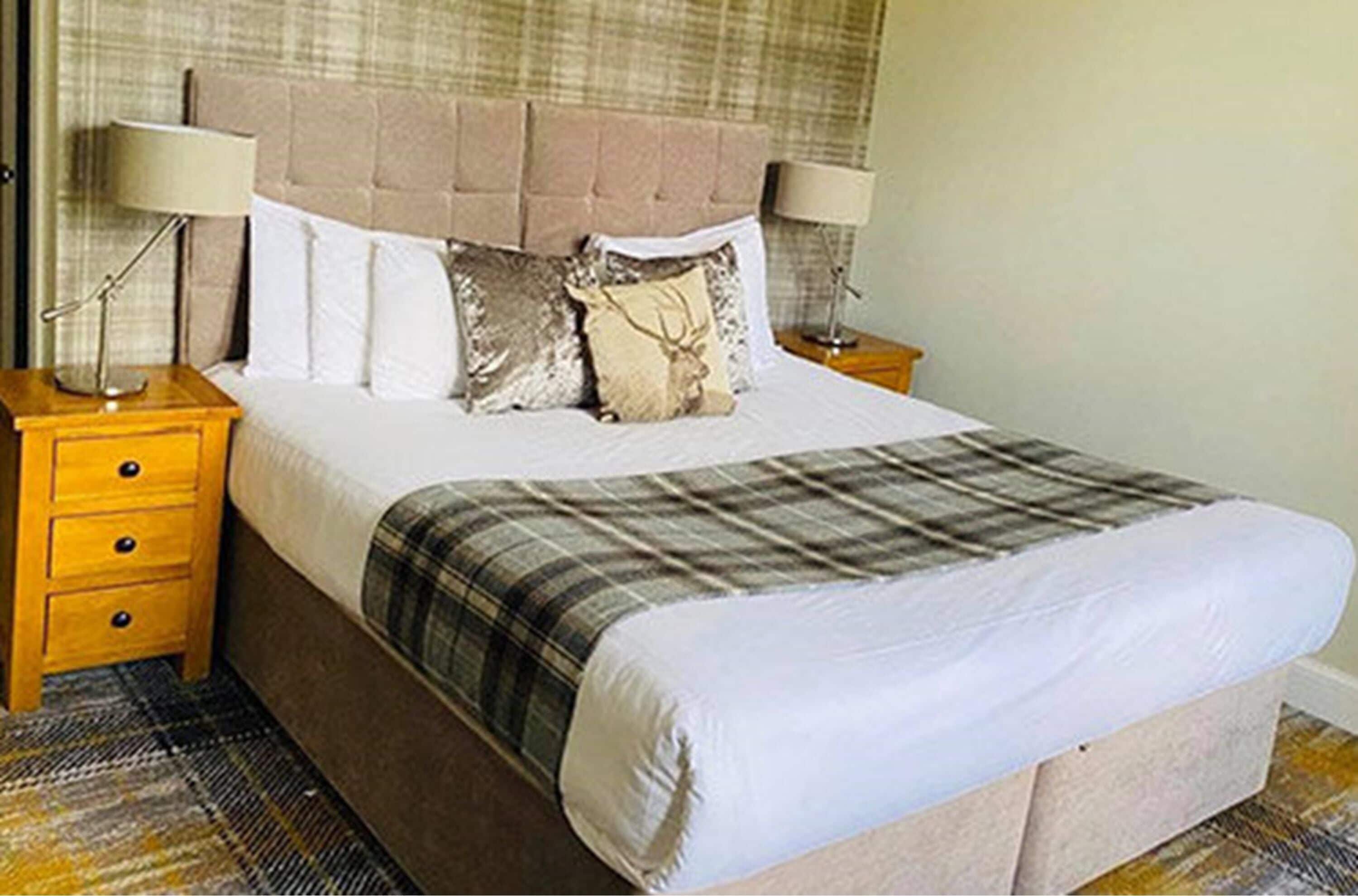 A neatly made bed with a plaid blanket, two bedside lamps, and a wooden nightstand with drawers.