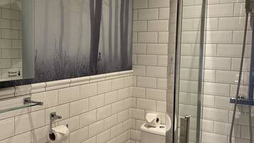 Un baño con azulejos blancos tipo metro, mampara de ducha de vidrio, inodoro blanco y lavamanos con espejo.