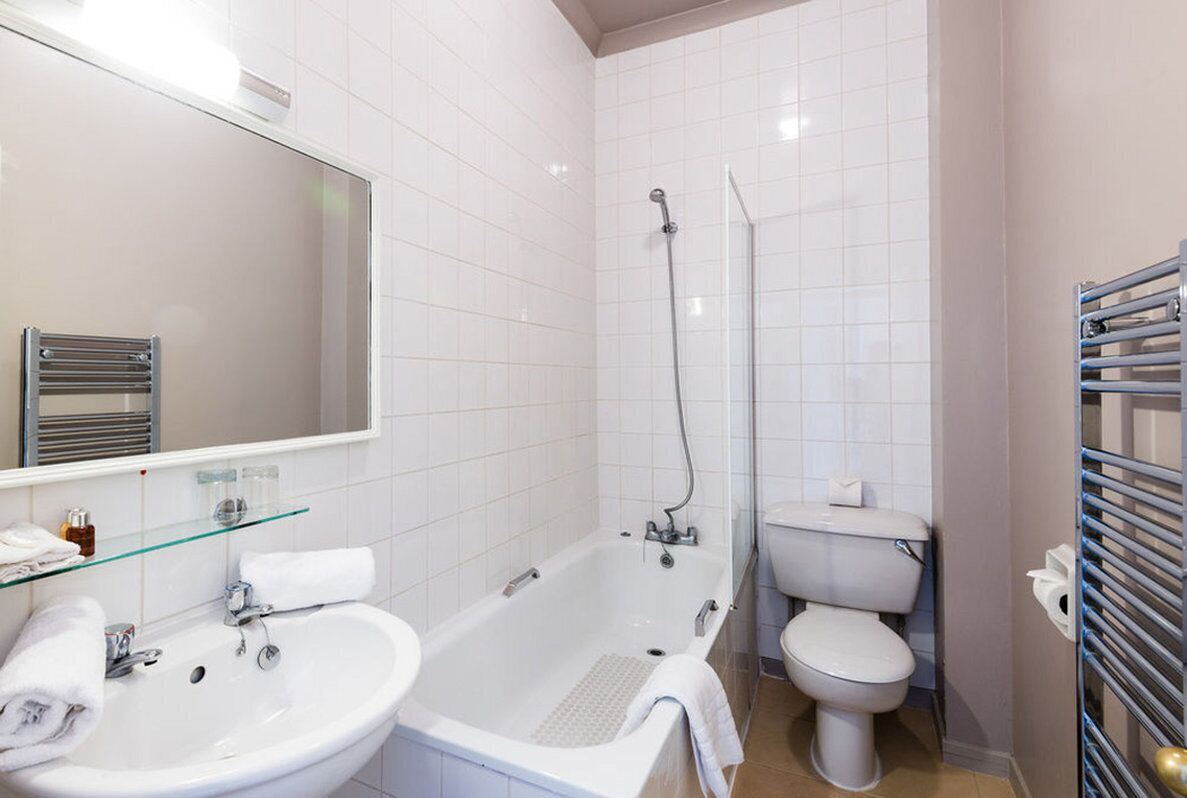 A bathroom with a white sink, glass shelf, and a bathtub.