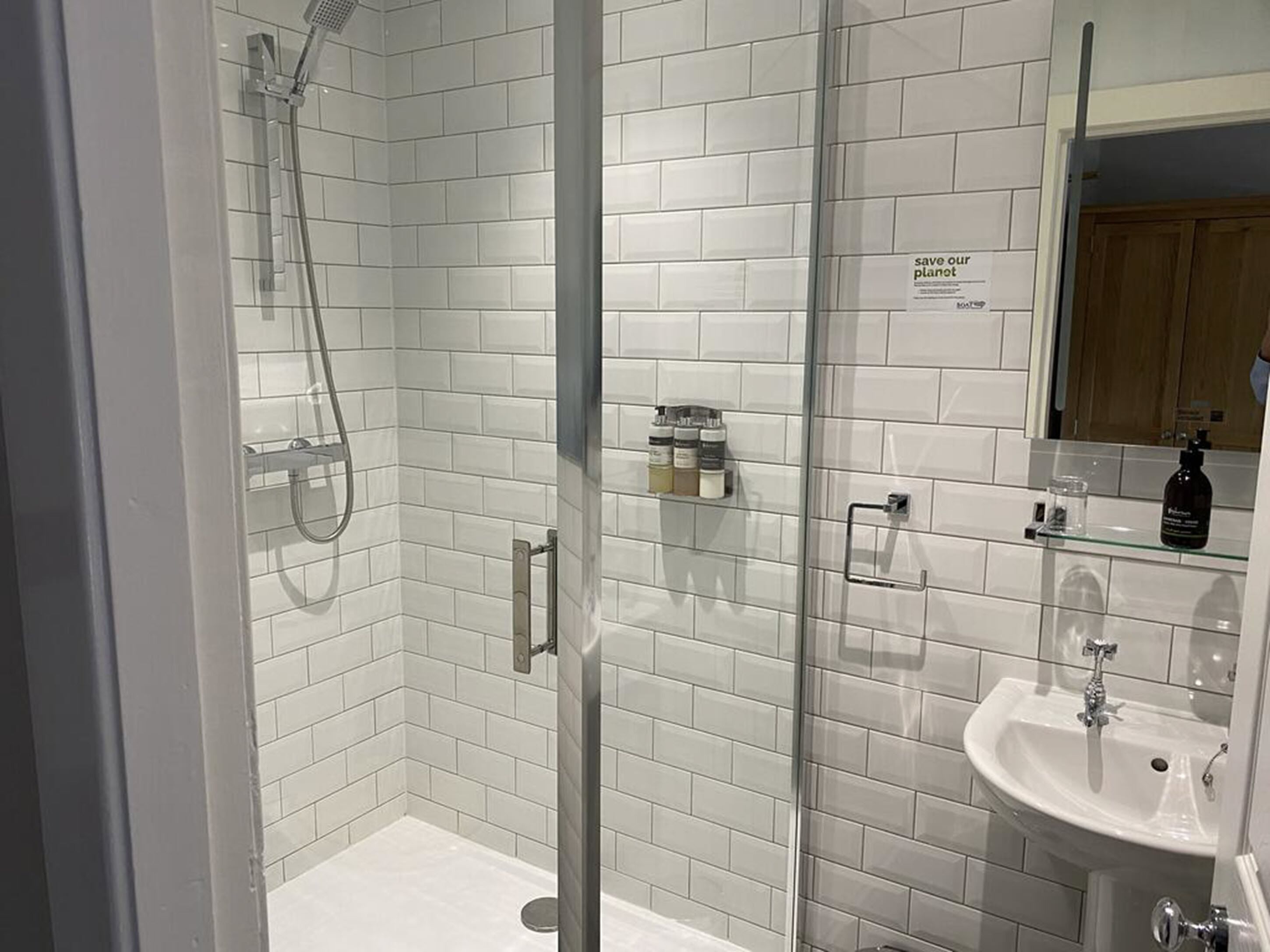 Une salle de bain moderne avec des carreaux de céramique blancs rectangulaires, une douche en verre, un lavabo et un miroir.