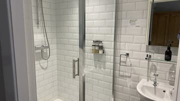 Un baño moderno con azulejos blancos tipo metro, cabina de ducha de vidrio, lavamanos y espejo.