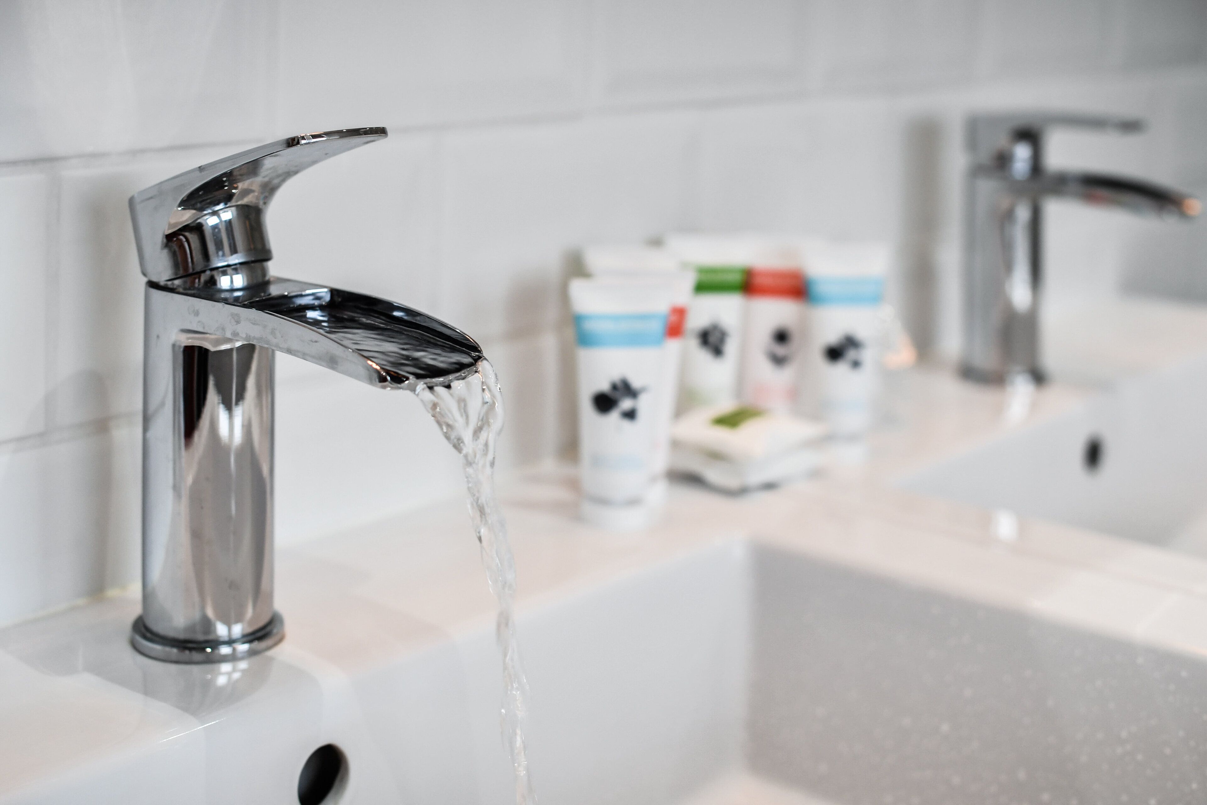 A modern bathroom with a chrome faucet and running water, a white sink, and a mirror.