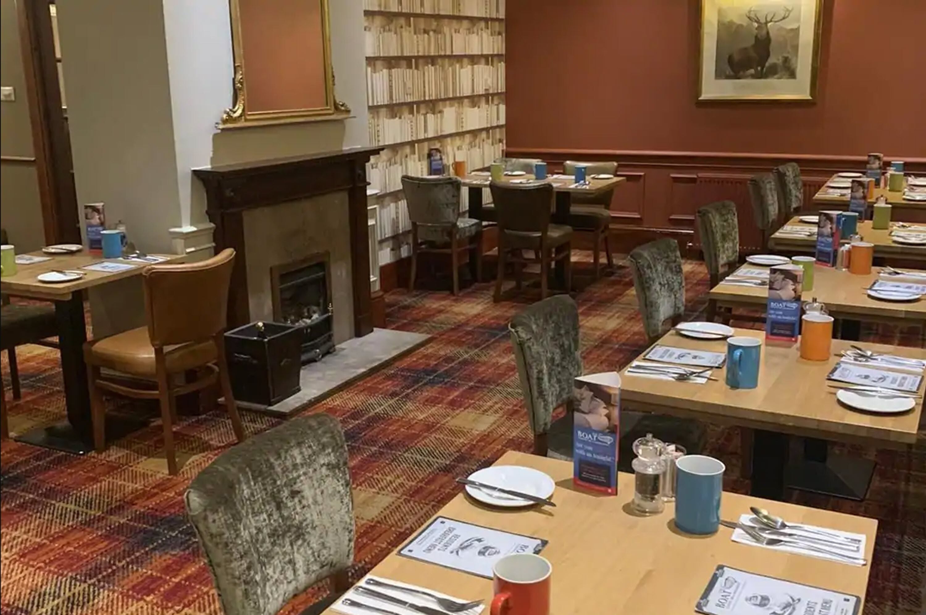 A dining area with tables set for a meal, a fireplace, and a bookshelf filled with books.