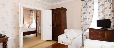 A room with a bed, a white sofa, a wooden coffee table, a TV on a wooden cabinet, and a wardrobe.