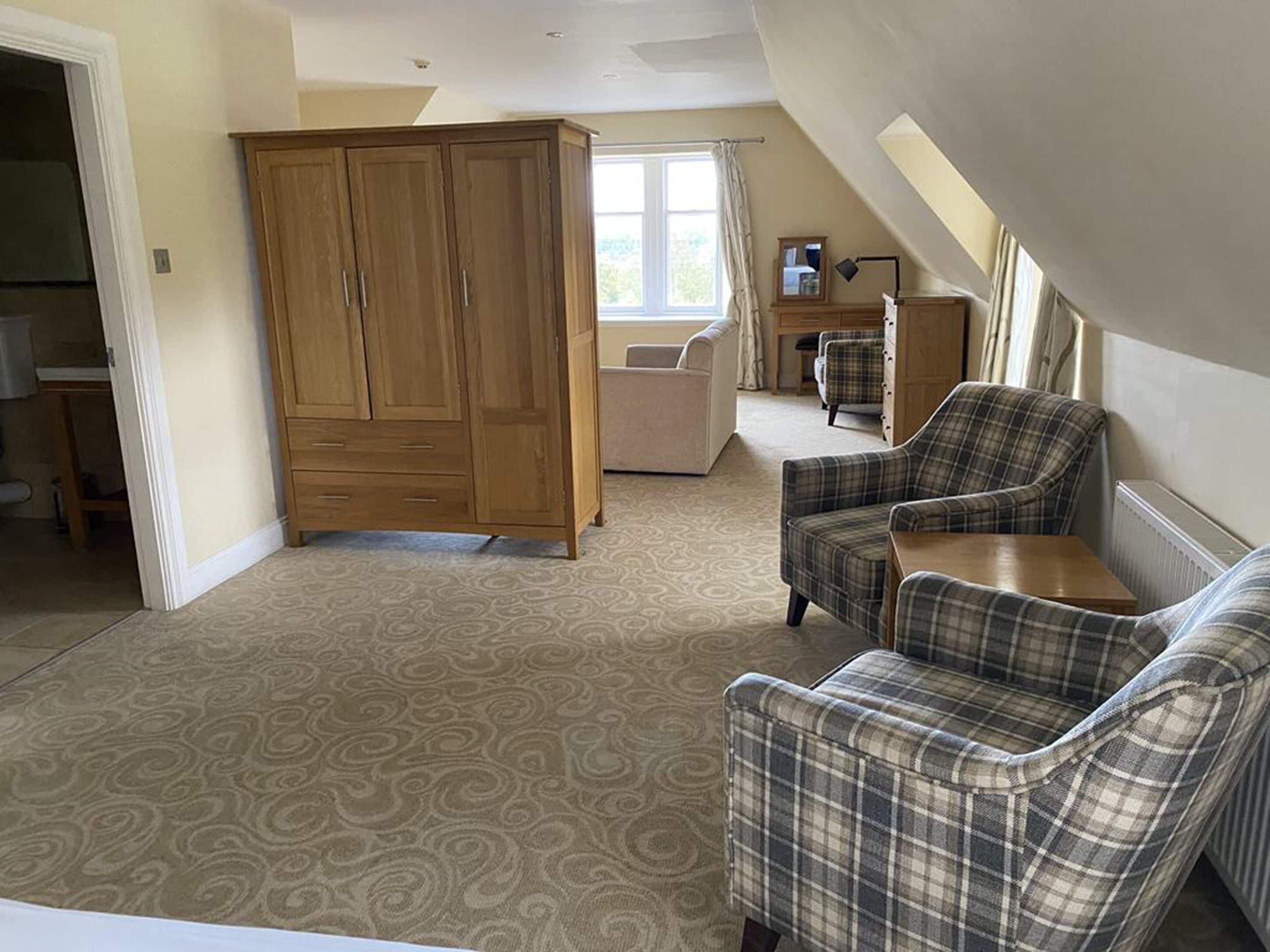 A spacious room with a large wardrobe, two plaid armchairs, a sofa, and a window with curtains.