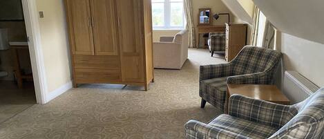 A spacious room with a large wardrobe, two plaid armchairs, a sofa, and a window with curtains.