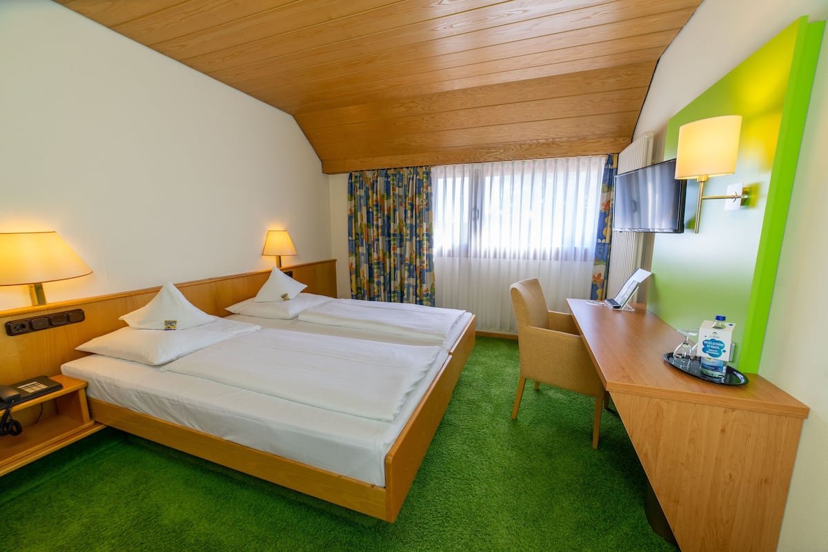 A hotel room with two beds, a desk, a chair, a TV, and a telephone.