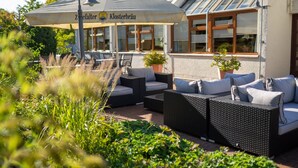An outdoor seating area with wicker furniture and a large umbrella. - Filderhotel (Ostfildern)