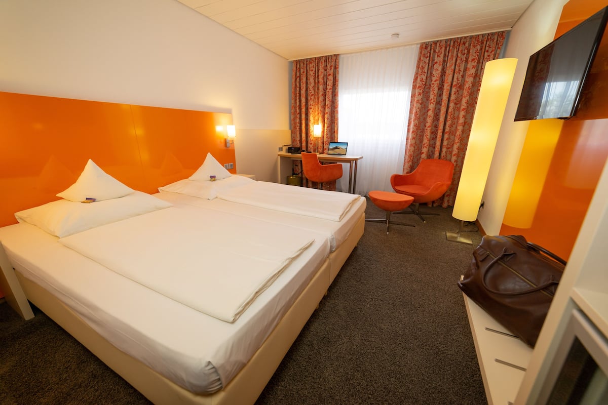 A hotel room with two beds, a desk with a laptop, a chair, a TV, and a brown bag on a dresser.