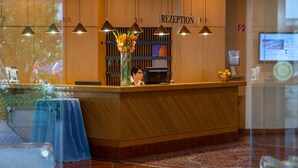 A reception area with a wooden reception desk, a computer, and a vase of flowers. - Filderhotel (Ostfildern)