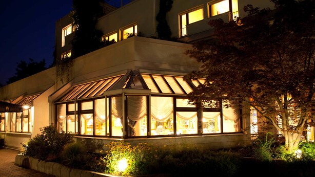A modern building with a large glass conservatory, surrounded by well-maintained gardens and a paved walkway. - Filderhotel (Ostfildern)