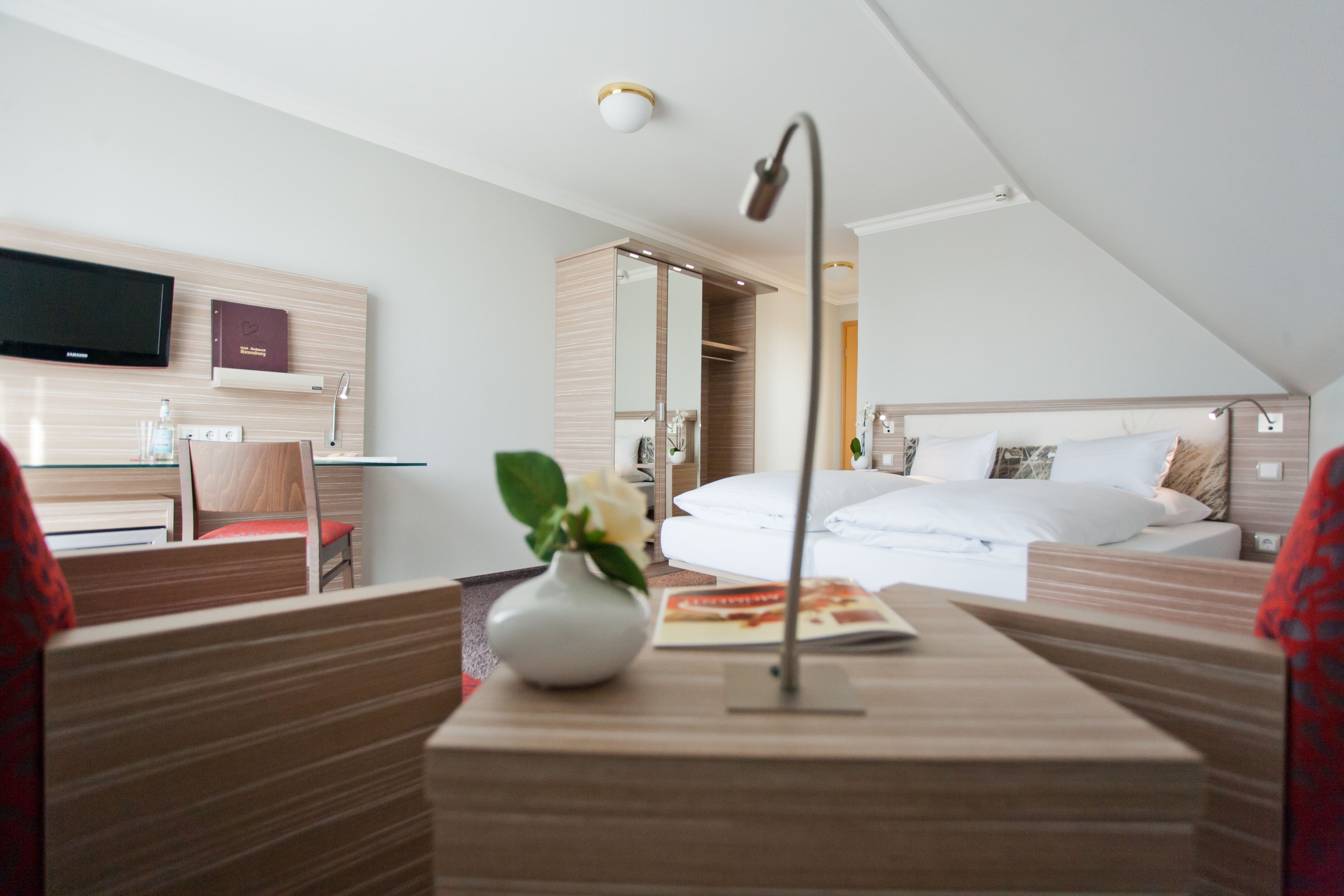 A modern hotel room with a bed, bedside table, and a TV mounted on the wall.