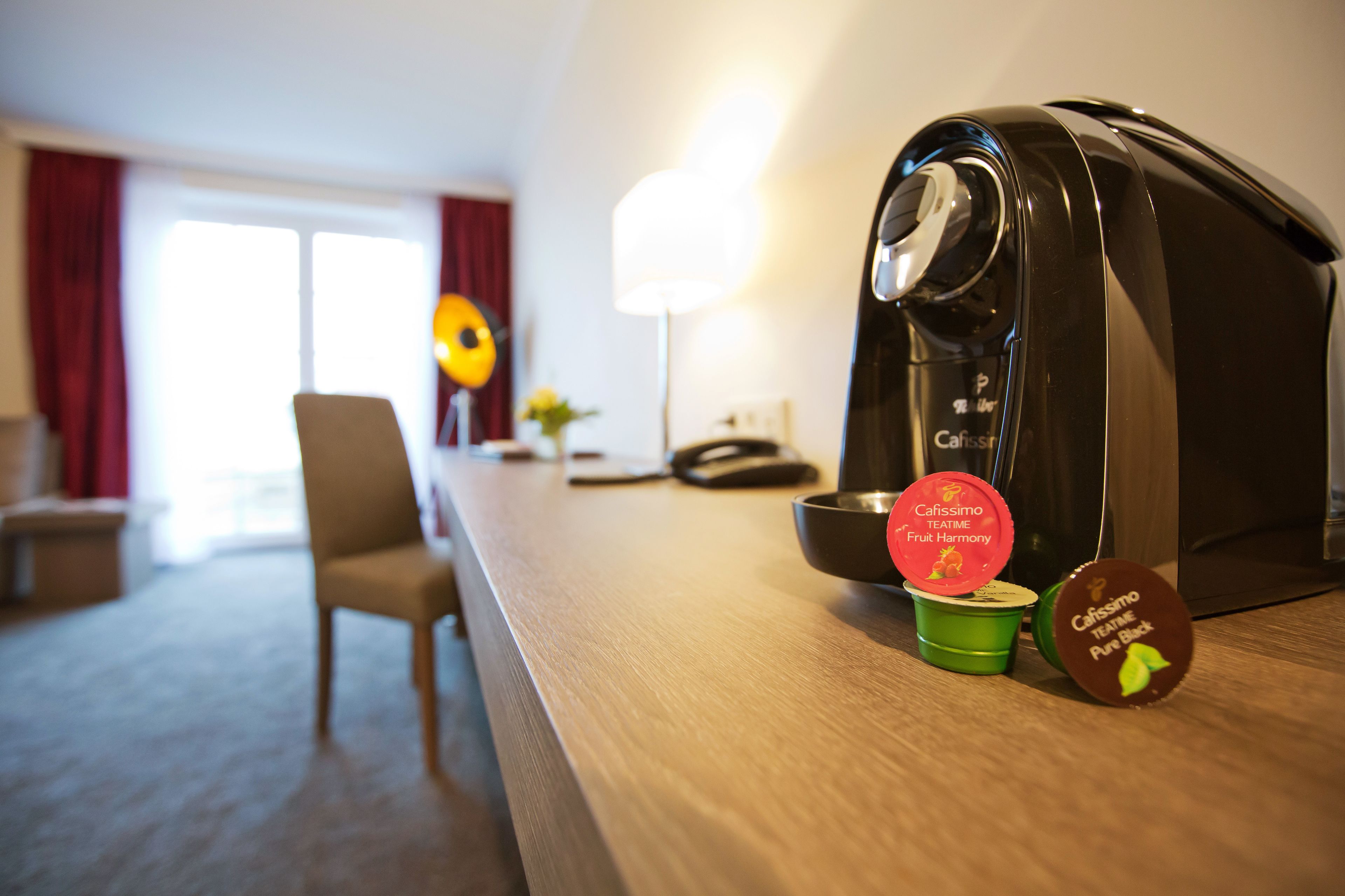 Une machine à café posée sur un comptoir en bois, avec deux dosettes de café étiquetées « Caffissimo Teatime Fruit Harmony » et « Caffissimo Teatime Pure Back ».