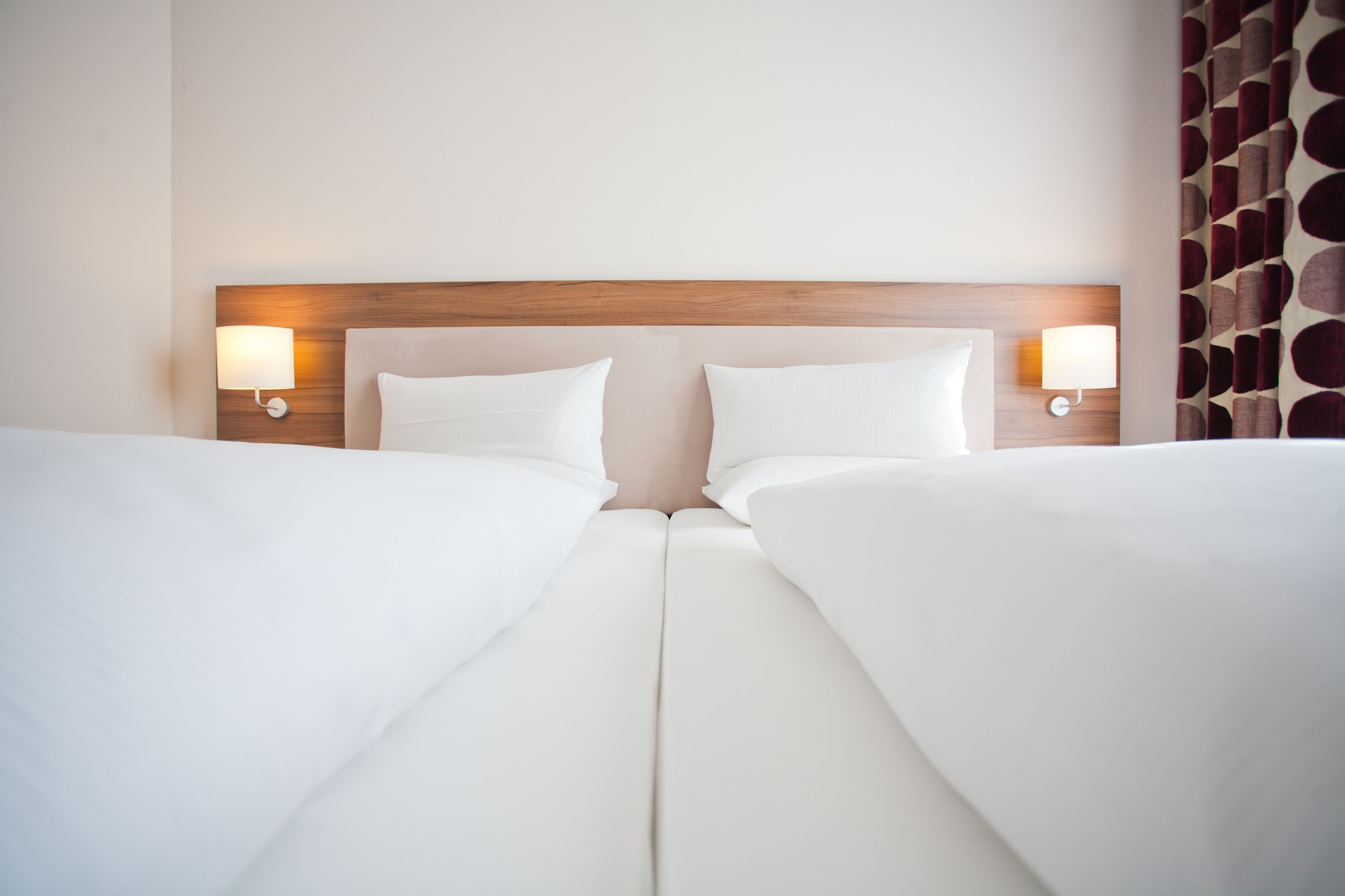 Habitación de hotel con cama doble, dos lámparas de noche y cabecera de madera.