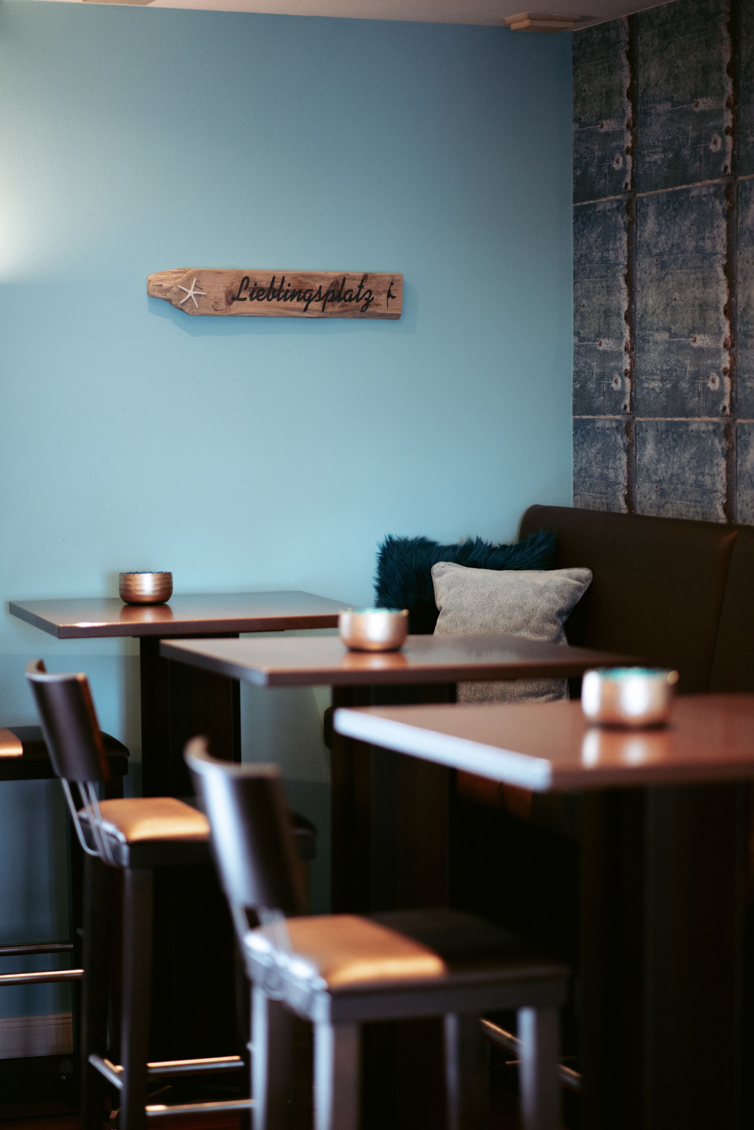 A restaurant interior with wooden tables and chairs, a blue wall, and a sign that reads "Lieblingsplatz".