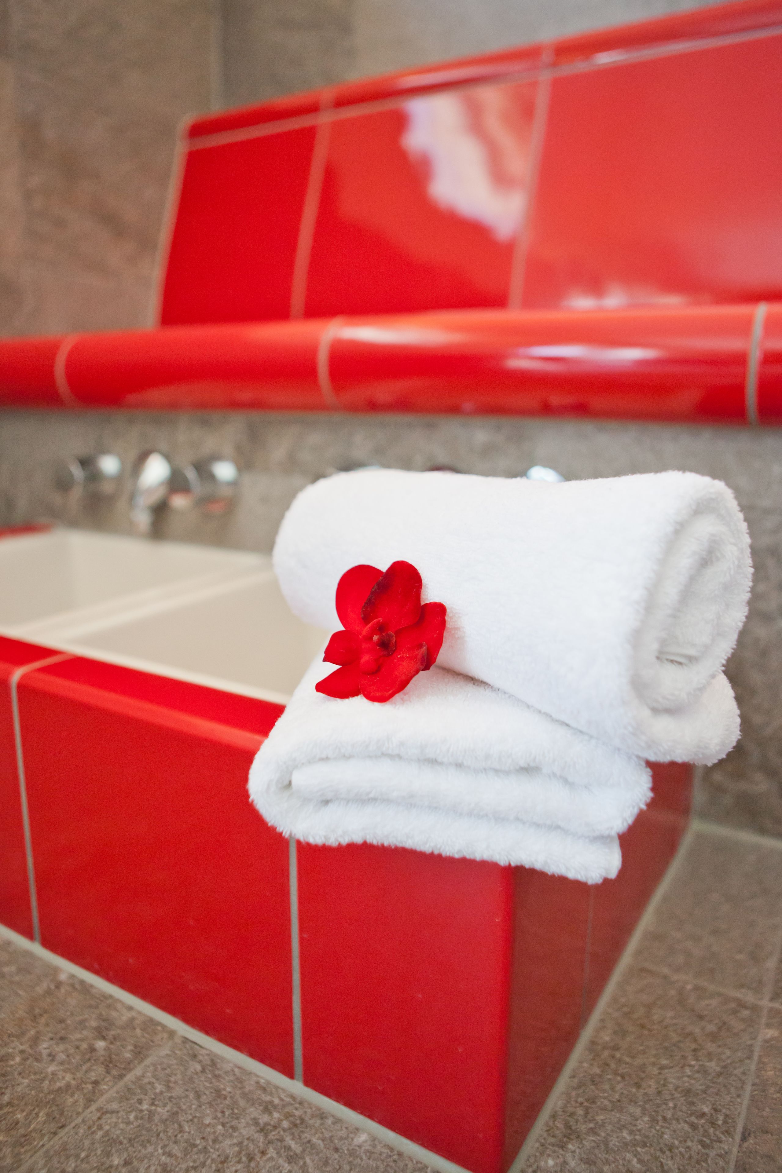 A red bathroom with a white towel stacked on a red towel warmer, a red flower decoration, and a white sink.