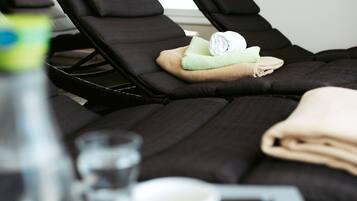 A room with two black massage chairs, a small table with a glass of water, a white cup, and a folded towel.