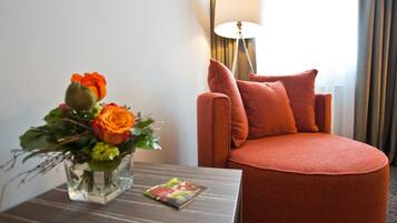 Ein Hotelzimmer mit einem runden orangefarbenen Sessel, einem kleinen Tisch mit Blumenvase und einer Lampe.