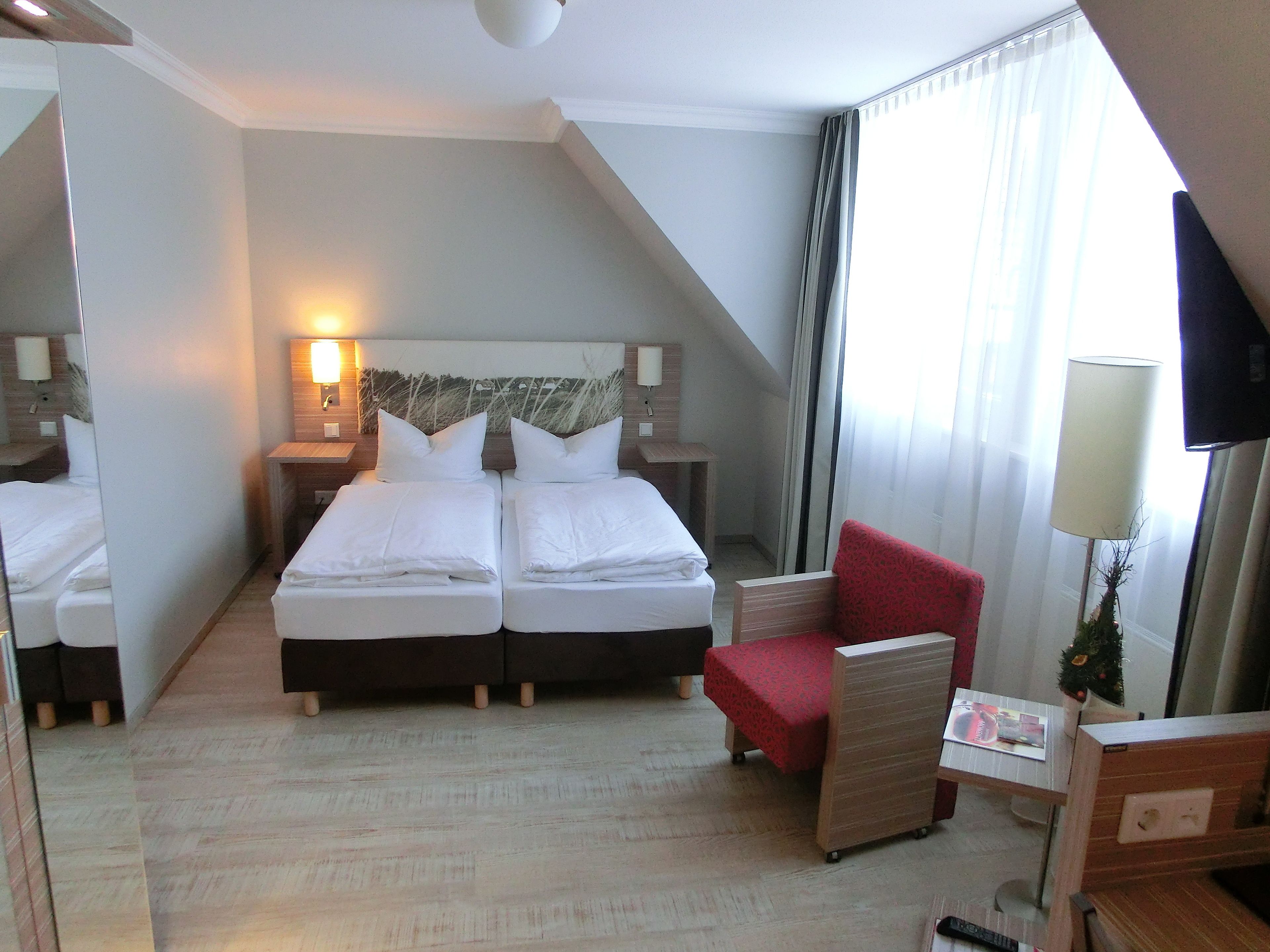 A hotel room with two beds, a red armchair, a small table, and a TV.