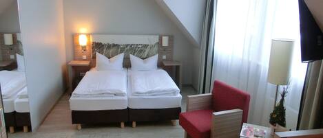 A hotel room with two beds, a red armchair, a small table, and a TV.