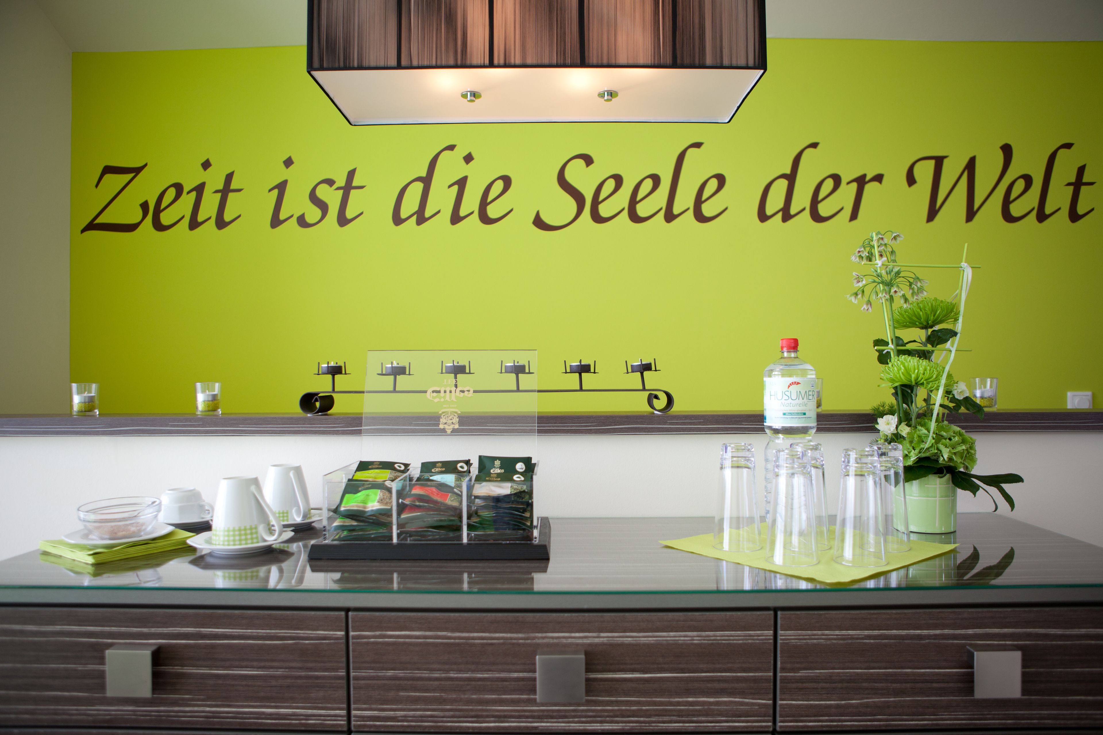 A reception area with a green wall and a clock. There are glassware and a plant on the counter.