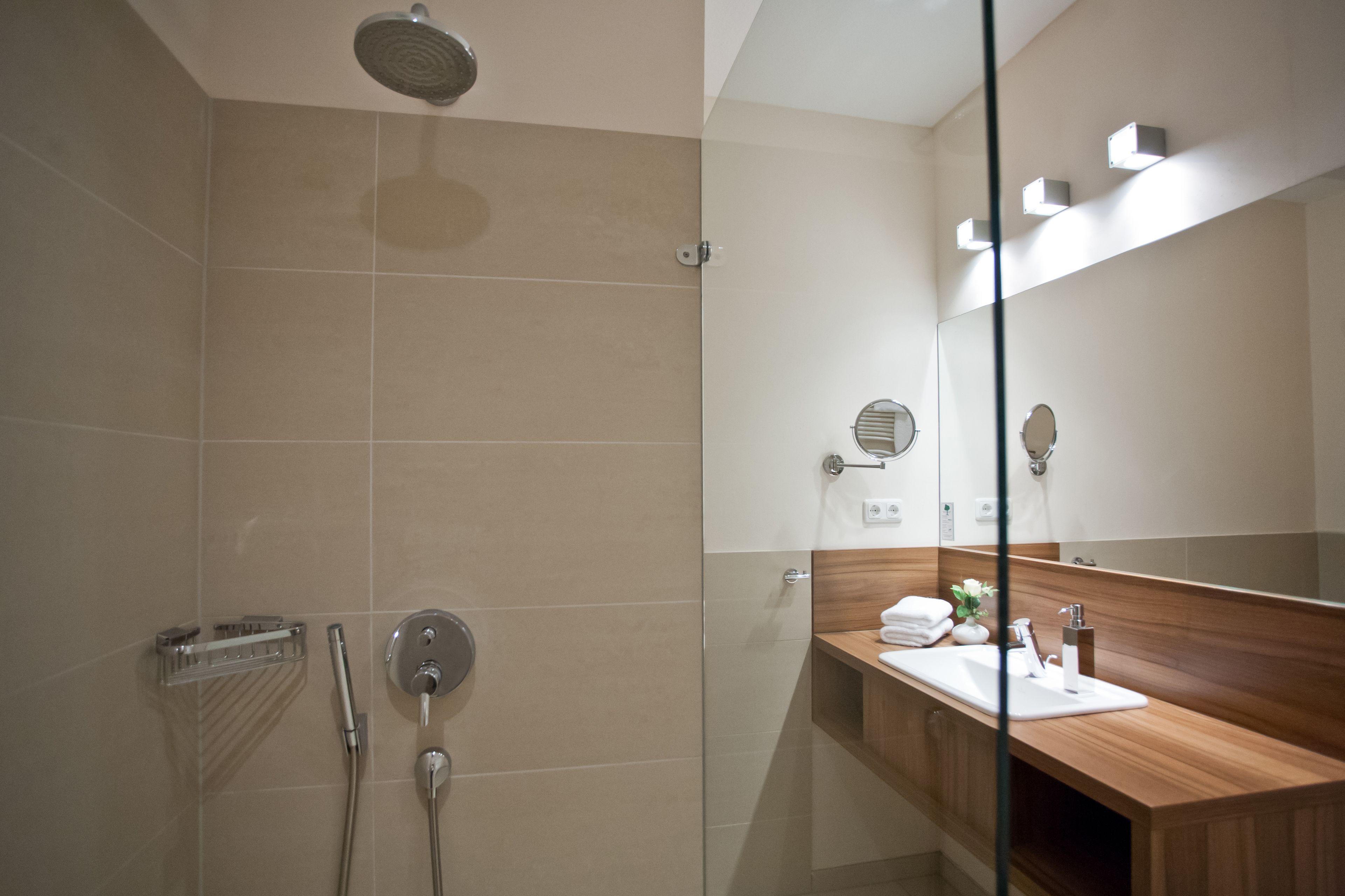 Un baño moderno con cabina de ducha de vidrio, tocador de madera y un espejo grande.