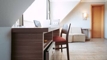 Una habitación moderna y compacta con escritorio, silla y un pequeño rincón de descanso.