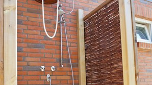 Una puerta de madera con un picaporte metálico, un cubo sujeto a la pared y un cabezal de ducha de metal.
