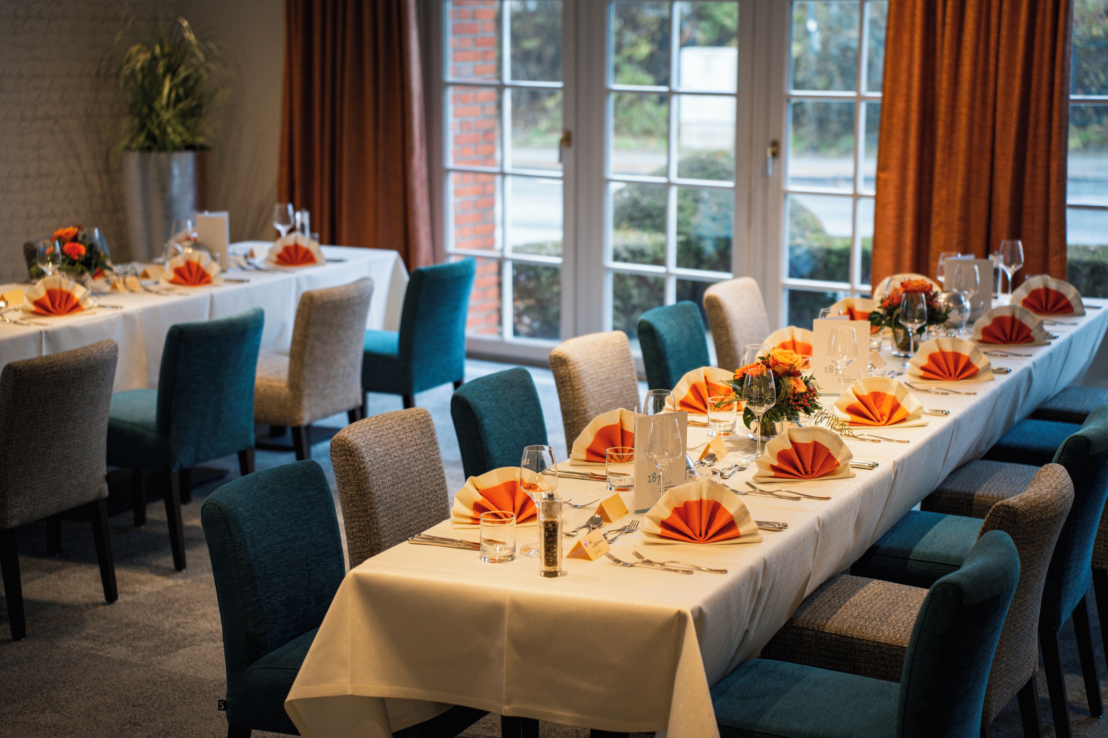 A dining area with tables set for a meal, chairs, and a view of the outdoors through large windows.