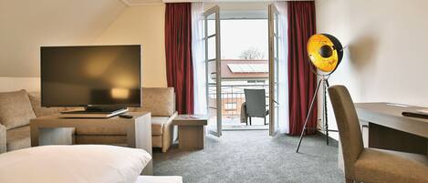 Habitación de hotel con cama, televisor, escritorio y una silla. Se ve el exterior por una puerta abierta.