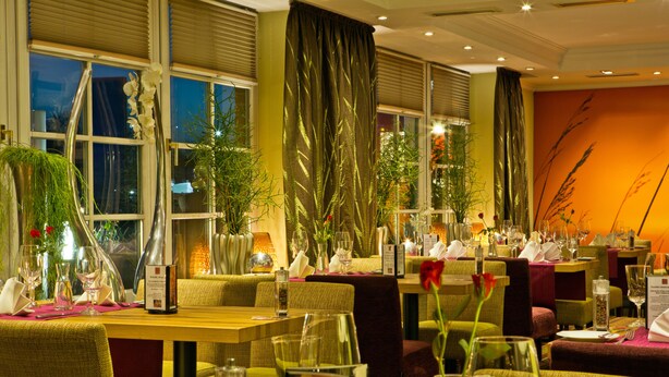 Un restaurante con varias mesas dispuestas para comensales, con cristalería transparente y centros de mesa florales.