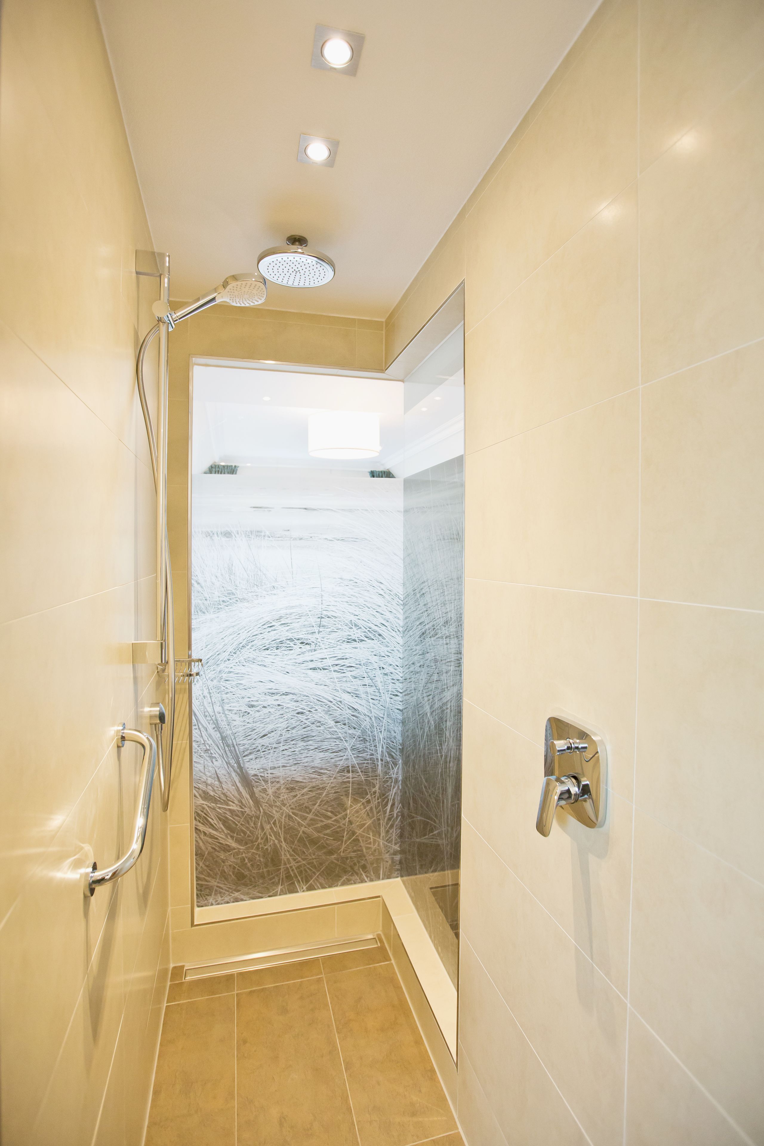 A modern shower with a glass door, a handheld showerhead, and a wall-mounted control.