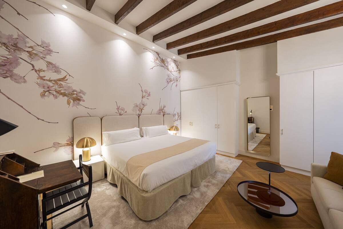 A bedroom with a large bed, bedside tables, a desk, a chair, a round table, and a mirror.