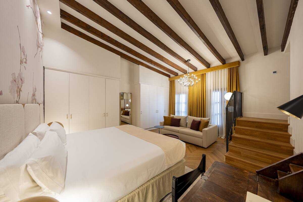 A modern bedroom with a large bed, a sofa, a small table, and a staircase.