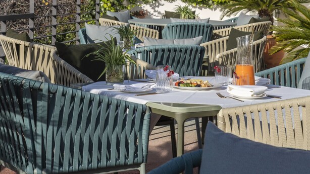 Um terraço com mesas ao ar livre, uma mesa de jantar posta com pratos e copos, e vista para um edifício histórico com arquitetura detalhada.