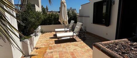 A rooftop patio with a tiled floor, a lounge chair, a sun umbrella, and a small grill.