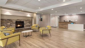 A lobby with a fireplace, yellow chairs, a reception desk, and a sign reading "WELCOME THE MOTHER OF STATES". - Hampton Inn Waynesboro/Stuarts Draft (Fishersville)