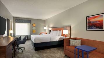A hotel room with a bed, a desk, a chair, a sofa, and a small table.