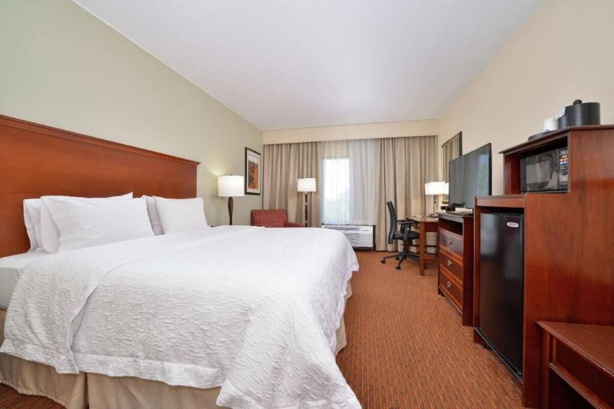 A hotel room with a large bed, a desk with a computer, a television, and a refrigerator.
