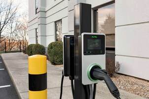 Estación de carga para vehículos eléctricos con pantalla digital, ubicada al aire libre cerca de un edificio.
