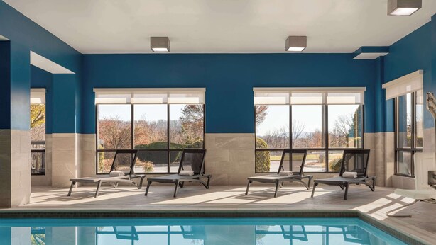 A swimming pool area with four lounge chairs and large windows offering a view of trees. - Hampton Inn Waynesboro/Stuarts Draft (Fishersville)
