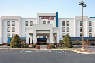 Un hotel Hampton Inn by Hilton con fachada moderna, estacionamiento y un área de entrada ajardinada.