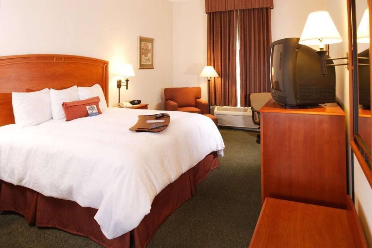 Ein Hotelzimmer mit einem großen Bett, einem Fernseher, einem Schreibtisch und einem Sessel.