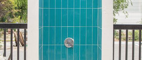 A blue-tiled shower enclosure with a metal faucet, surrounded by a white wall and a black metal fence.