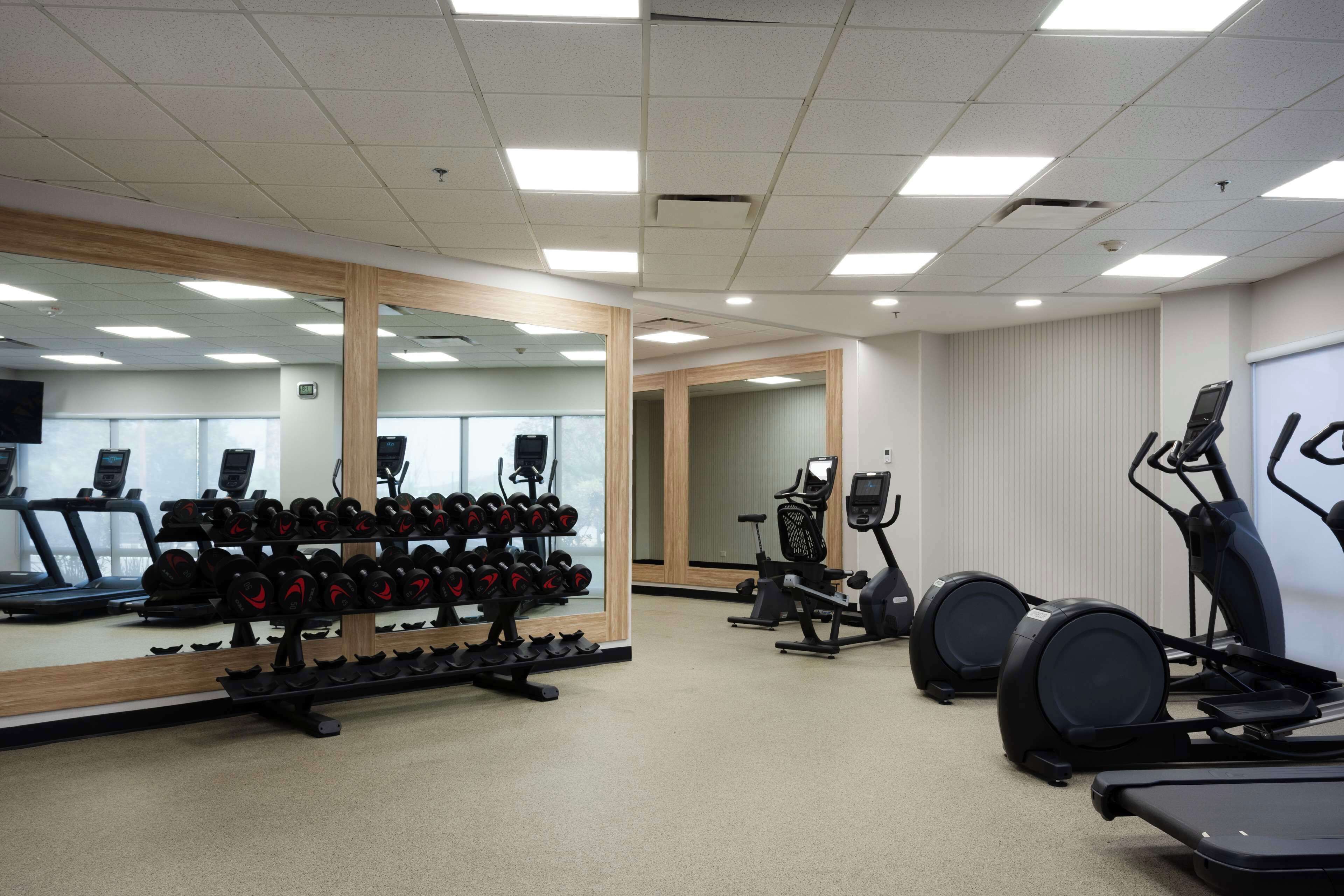 Ein Fitnessstudio mit Laufbändern, Crosstrainern und einer Spiegelwand.