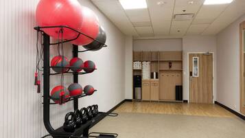 Un gimnasio con equipo de ejercicio, incluyendo kettelbells y balones medicinales, y un aparador de madera al fondo.