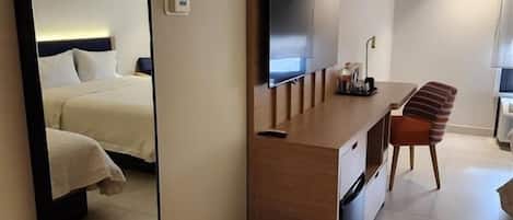Ein Hotelzimmer mit einem Bett, einem Schreibtisch mit Stuhl, einem Fernseher und einem großen Spiegel.
