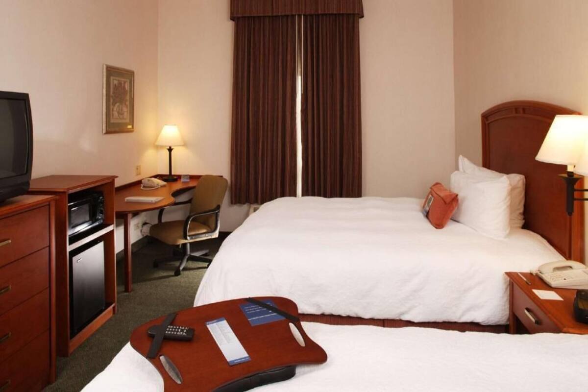 Ein Hotelzimmer mit Bett, Schreibtisch, Stuhl, Fernseher und einer kleinen Küchenzeile.