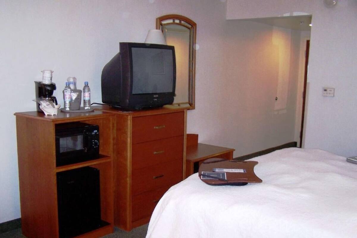 Ein Hotelzimmer mit einem Bett, einem Holzschrank mit Fernseher, einer Mikrowelle und einem kleinen Kühlschrank.
